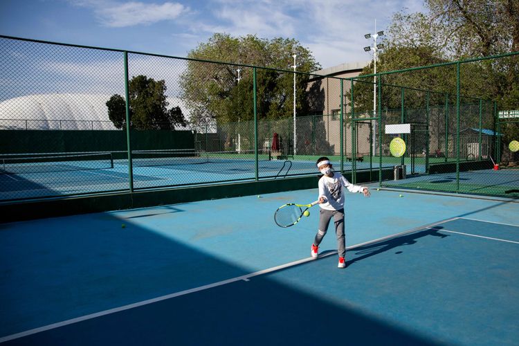 4月22日,天坛体育活动中心室外网球场,小学员在教练的指导下打网球.