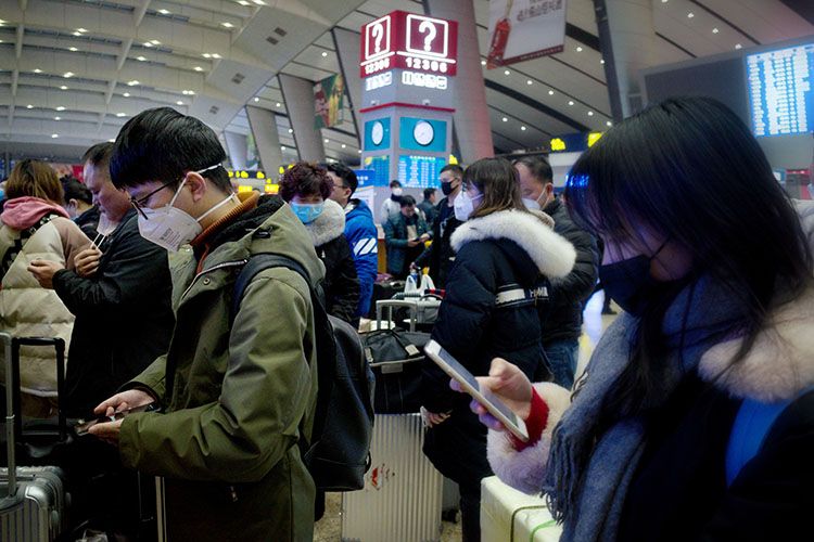 排队候车的旅客们戴着口罩,低头翻阅手机信息.